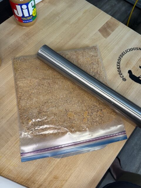 Crushing nutter butter cookies in a ziptop bag with a rolling pin on a wooden cutting board.