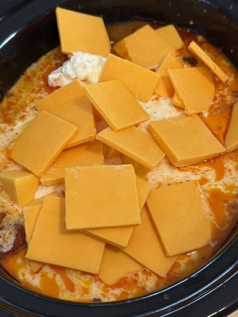 Adding the sour cream, heavy cream, Velveeta cheese and condensed soup to the slow cooker pot.