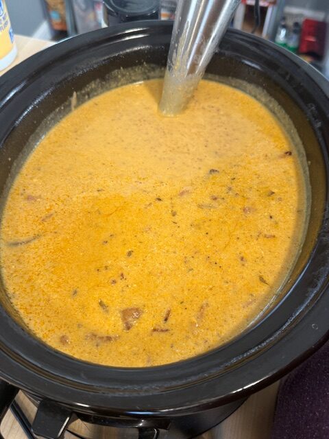 A ladle is in a pot of finished slow cooker cheesy potato soup.