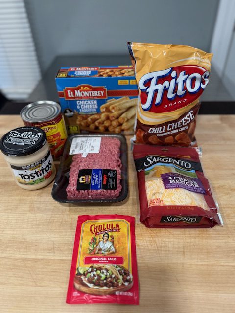 Ingredients displayed for lazy enchilada casserole. Fritos, ground beef, shredded cheese, queso, taquitos, enchilada sauce, and taco seasoning.