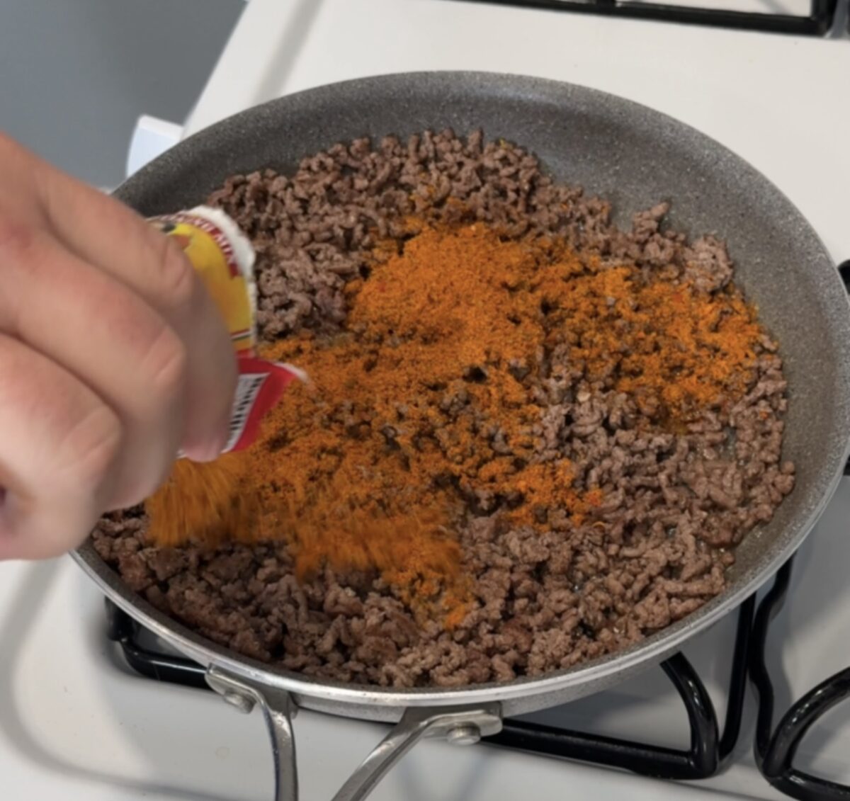 Adding taco seasoning from the packet to browned ground beef in a large nonstick skillet on the stove.