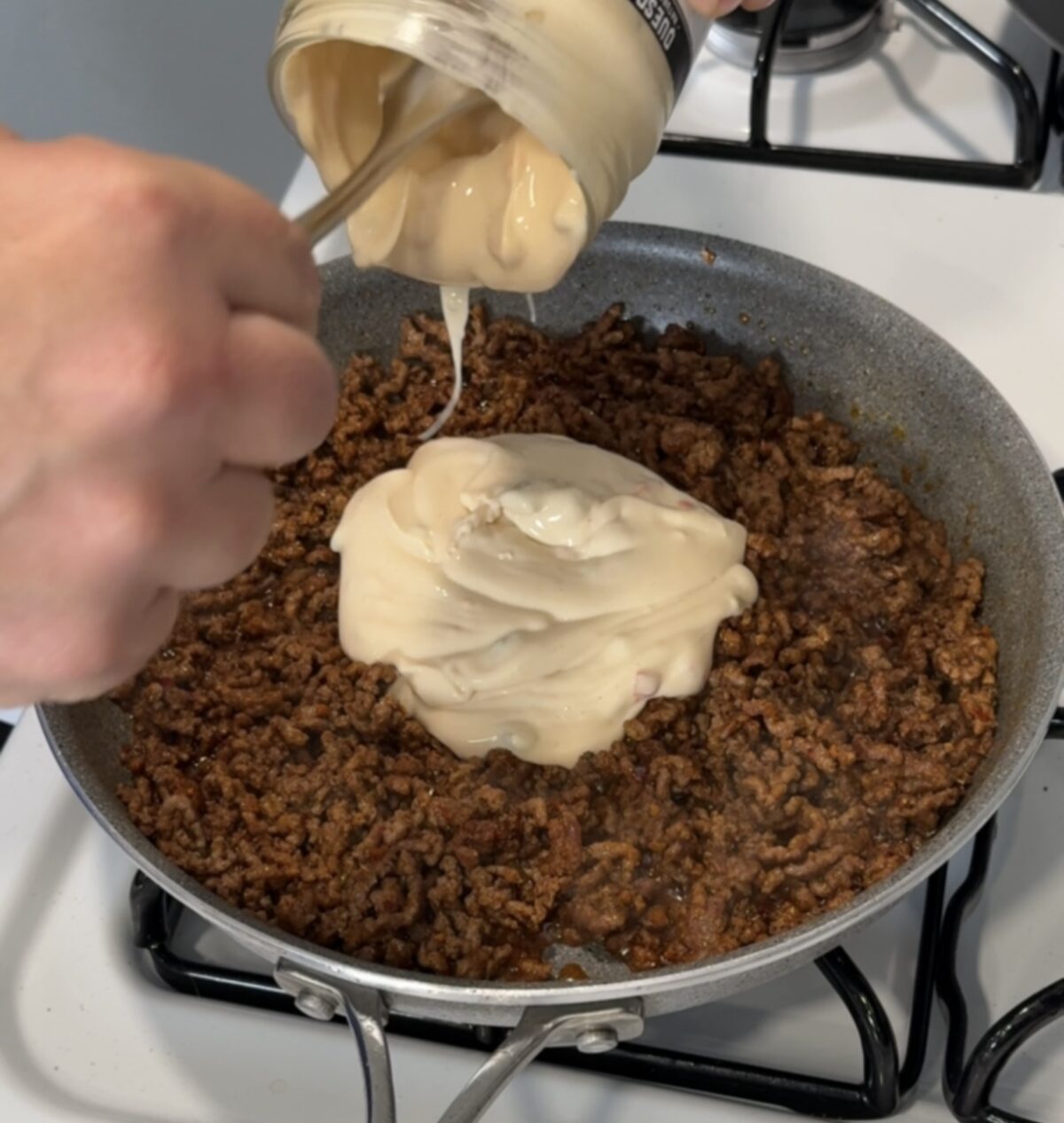 Queso from the jar is added to ground beef in a large nonstick skillet on the stove. 