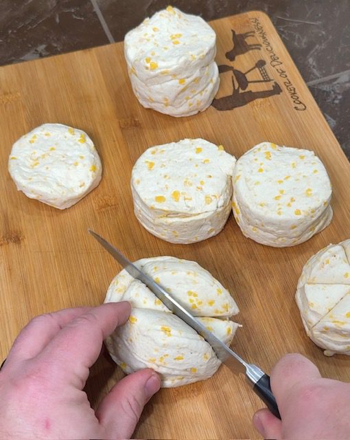 Biscuits on a cutting board being cut into quarters with a knife.