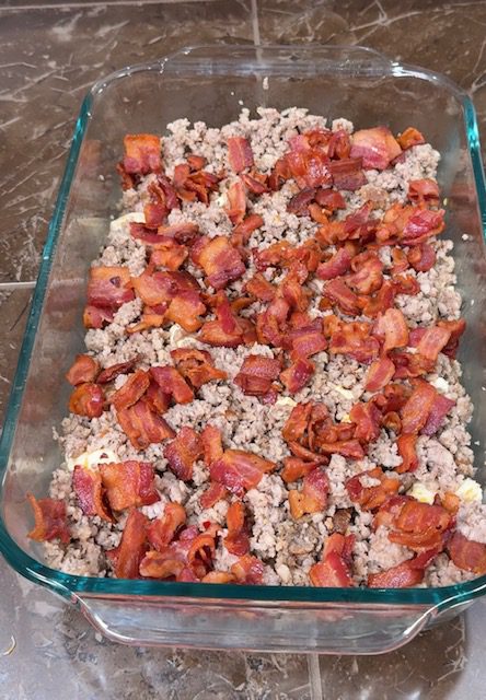 Layering Biscuits, sausage, and bacon in a glass baking dish.