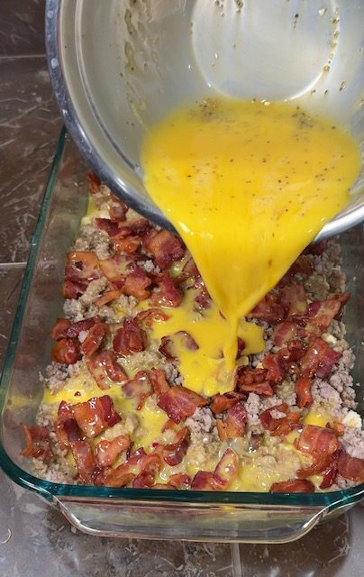 Pouring beaten eggs over ingredients layered in baking dish.