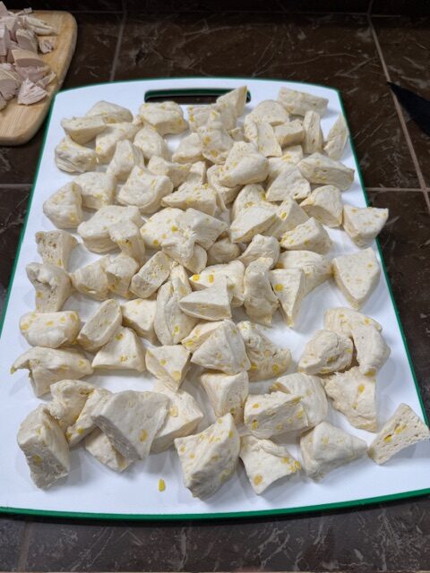 Canned jumbo biscuits are cut into small pieces and spread on a white cutting board. 