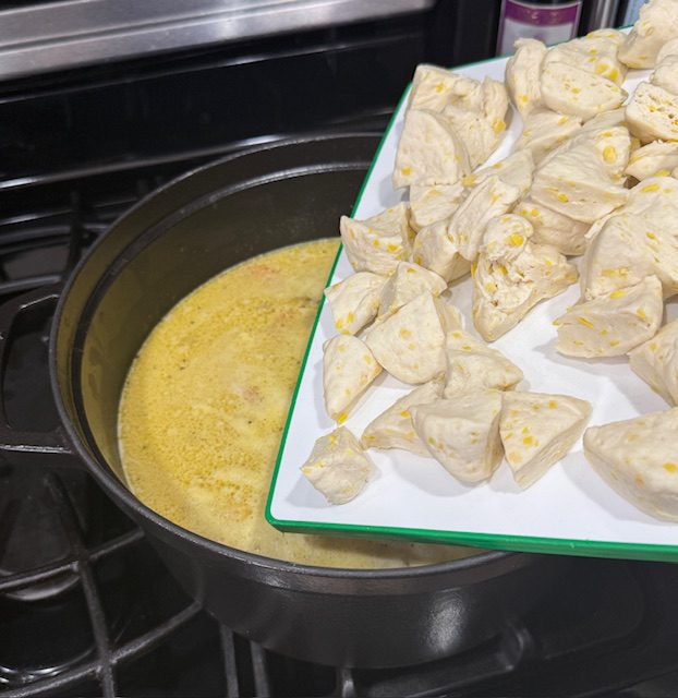 Biscuits on the white cutting board and being dropped into the simmering chicken and dumplings pot. 