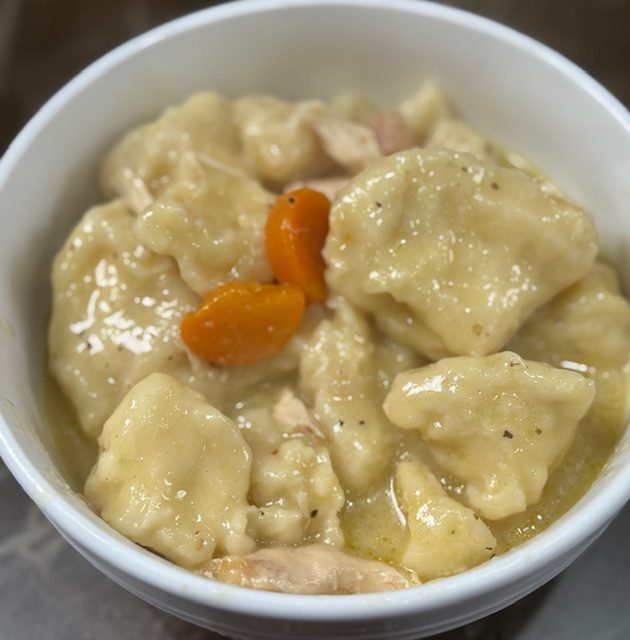 Chicken and dumplings with biscuits are plated in a white bowl.