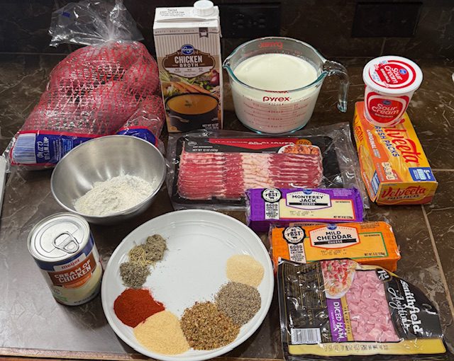 Ingredients for cheesy potato soup on a black counter. Potatoes, spices, bacon, cheddar cheese, Velveeta cheese, Monterey Jack cheese, condensed soup, sour cream, chicken stock, and heavy cream.