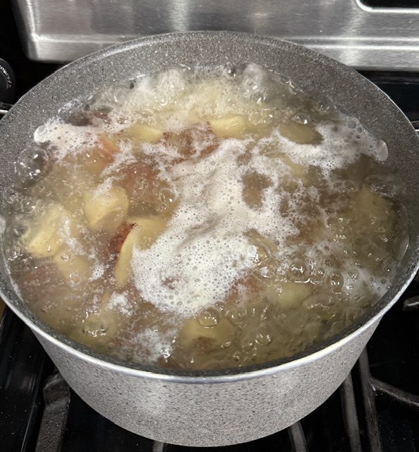 Red potatoes are boiling in a stainless pot of water.