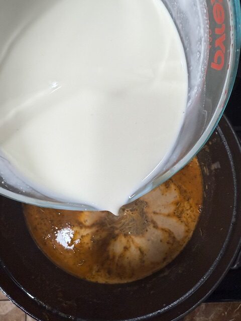 Heavy cream, cream of chicken soup, and sour cream in a measuring cup are ready to be added to the soup in a large black pot. 