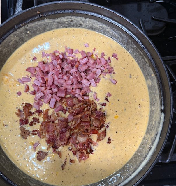 Ham, bacon, and the boiled potatoes are stirred back into the cheesy soup base in the pot. 