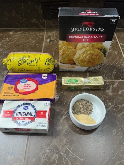 Ingredients for Red Lobster Sausage Balls displayed on a table. The ingredients include Red Lobster Cheddar Bay Biscuits, loose sausage, sharp cheddar cheese, cream cheese, butter, garlic powder, salt and pepper.