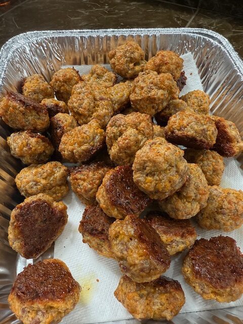 Finished old bay sausage balls are cooked and placed on top of a paper towel in a foil baking dish.