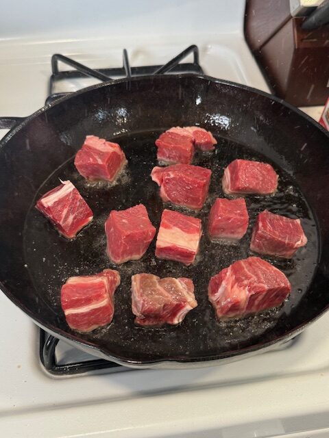 A cast iron skillet is searing steak bites.