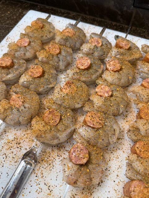 Shrimp and sausage skewers and laying on a cutting board and sprinkled with creole seasoning.