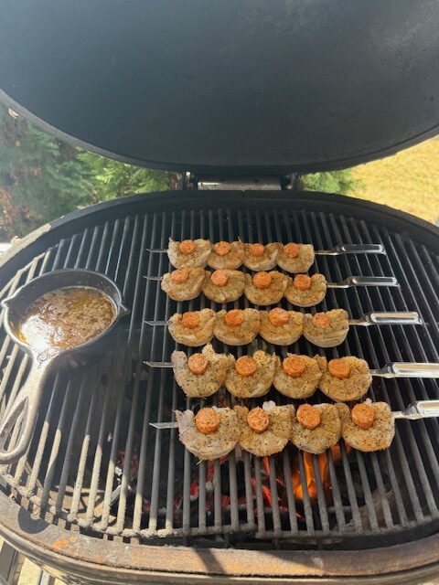 Shrimp and sausage skewers are on a grill outside.