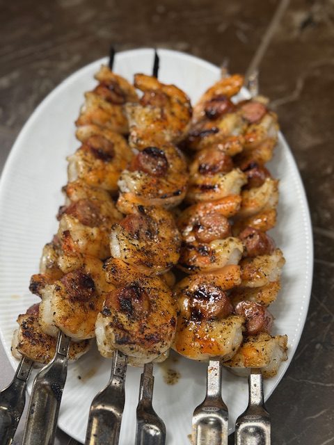 Finished shrimp and sausage skewers on a white plate.
