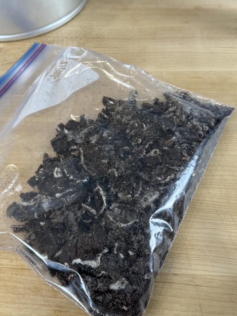 Oreos are crushed in a large zip top bag on a wooden counter.