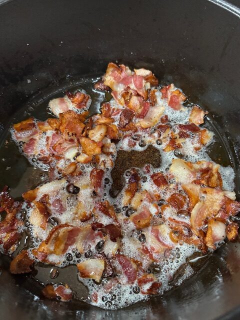 Bacon is cooking in bottom of Dutch oven. 