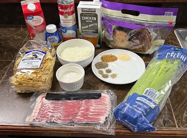 Ingredients displayed for creamy chicken noodles. Includes noodles, abcon, chicken, spices, celery, romano cheese, cream, condensed soup, carrots, and chicken broth. 