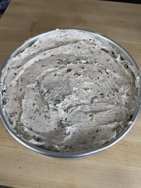 The no-bake Oreo cheesecake filling is spread into the spring form pan. The pan is set on a wooden counter.