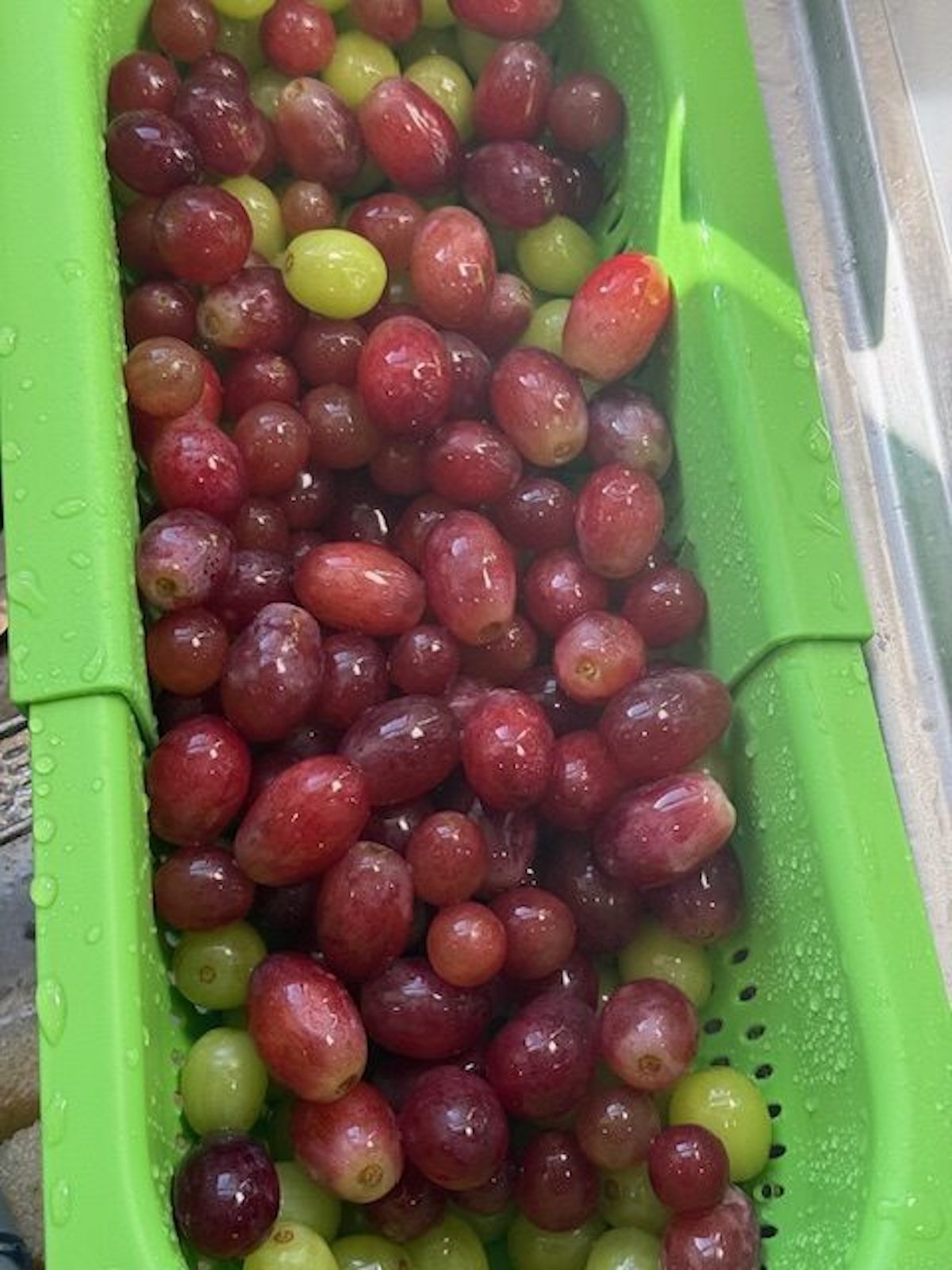 Washing red and green grapes in a green colander.