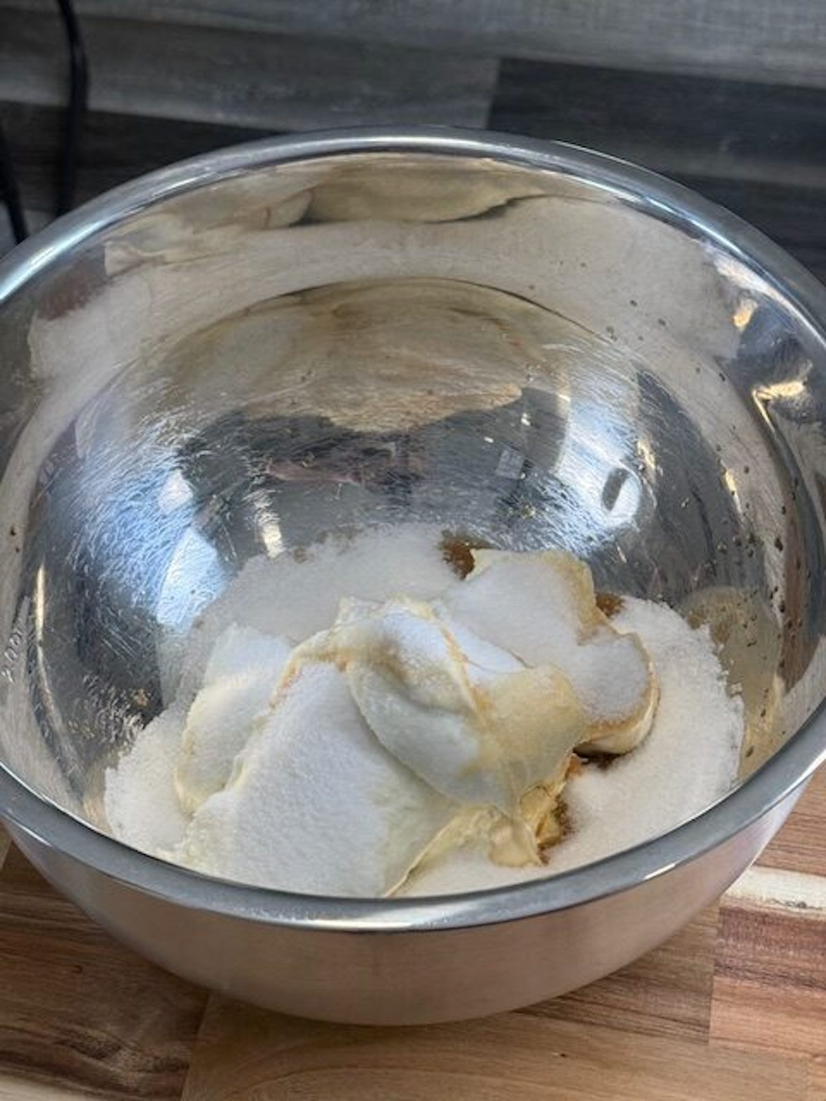 A metal mixing bowl with sugar, cream cheese, and vanilla.
