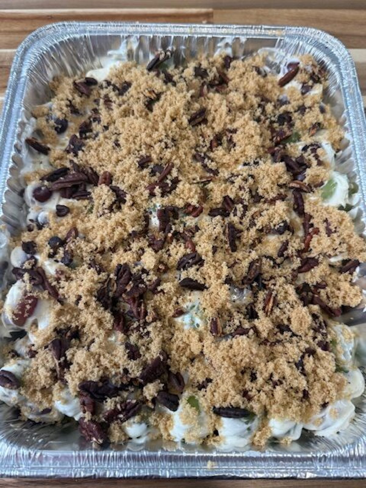 Grape salad in a foil pan is topped with brown sugar and pecans.