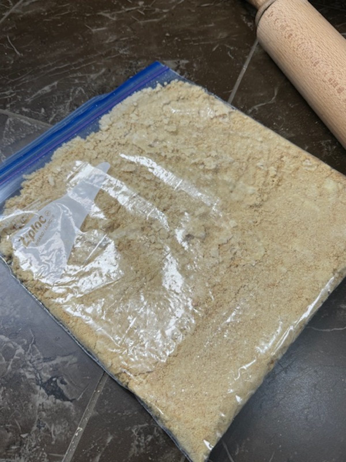 Crushed vanilla cookies in a zip-top bag with a rolling pin in the background.