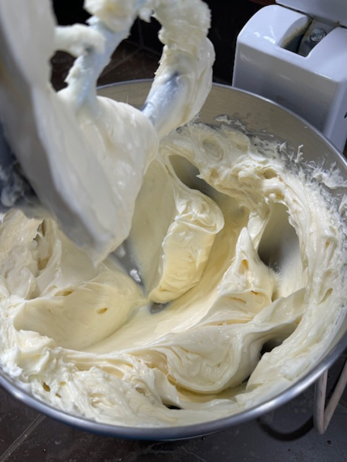 A stand mixer with the paddle attachment is mixing the cream cheese and sour cream.