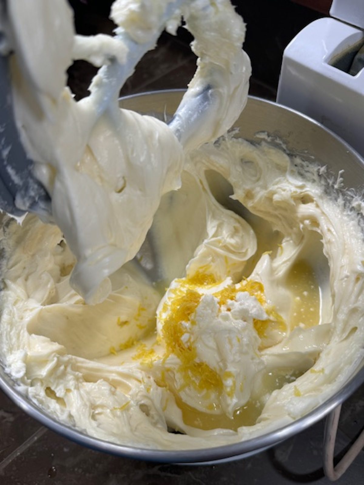 A stand mixer with the paddle attachment is mixing the cheesecake batter with lemon zest and juice on top.
