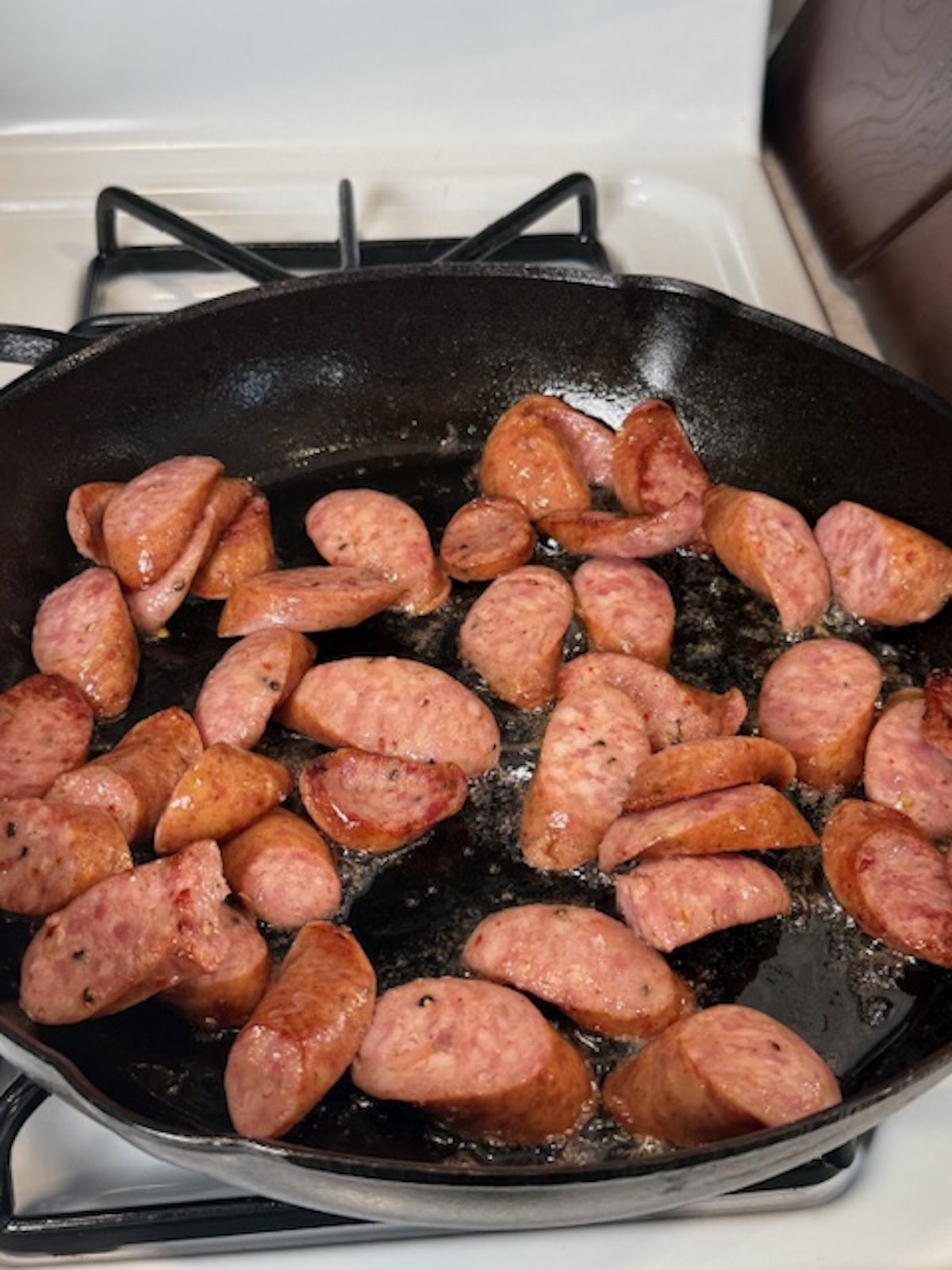 Smoked sausage browning in a cast iron skillet.