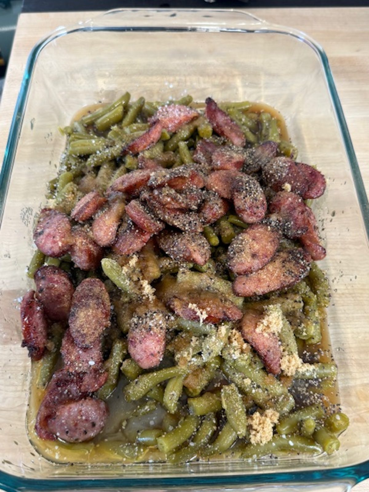 Green beans and smoked sausage in a glass baking dish before baking.