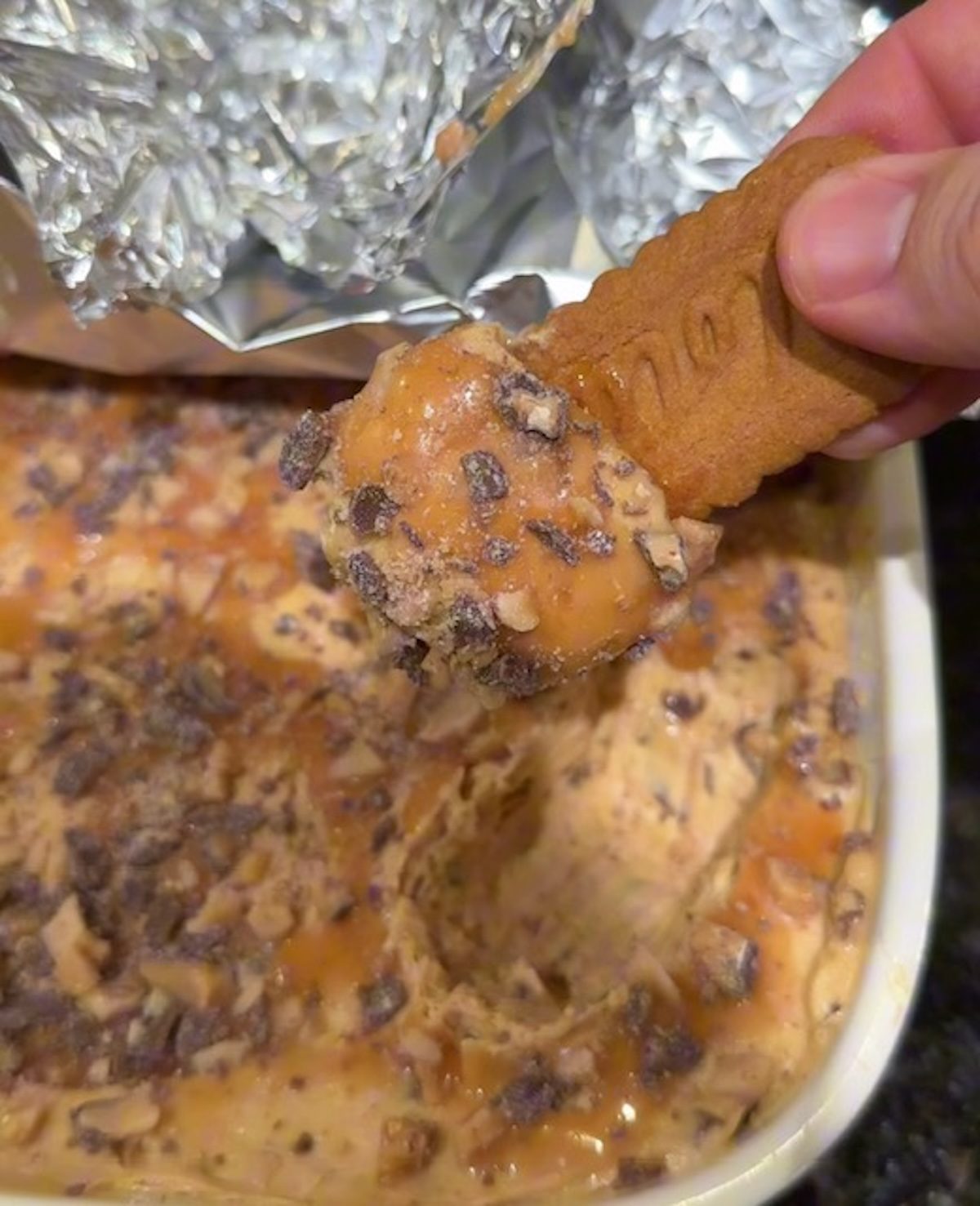 A Biscoff cookie being dipped into Biscoff cookie butter dip by a hand.