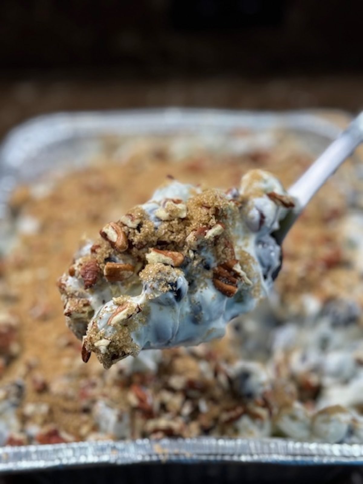 Grape salad is being lifted by a spoon from a metal pan.