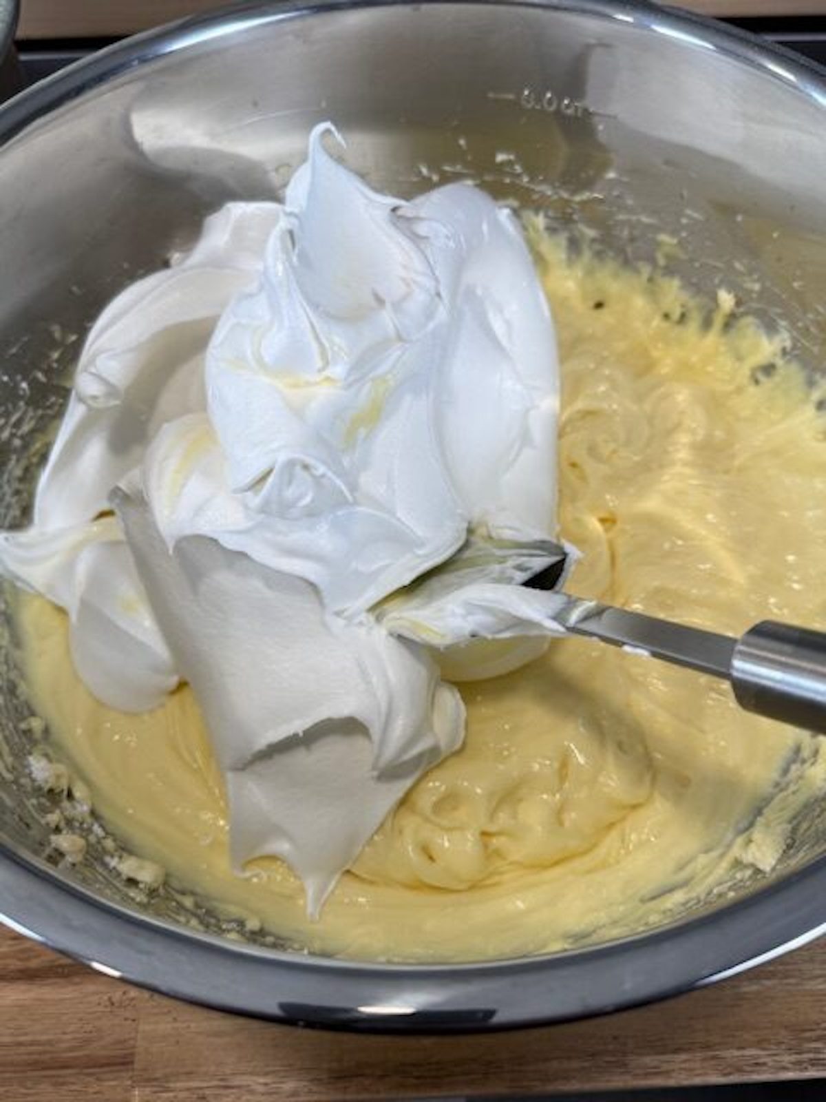 Whipped topping is added to a large metal bowl with cream cheese mixture. A spatula is in the bowl.