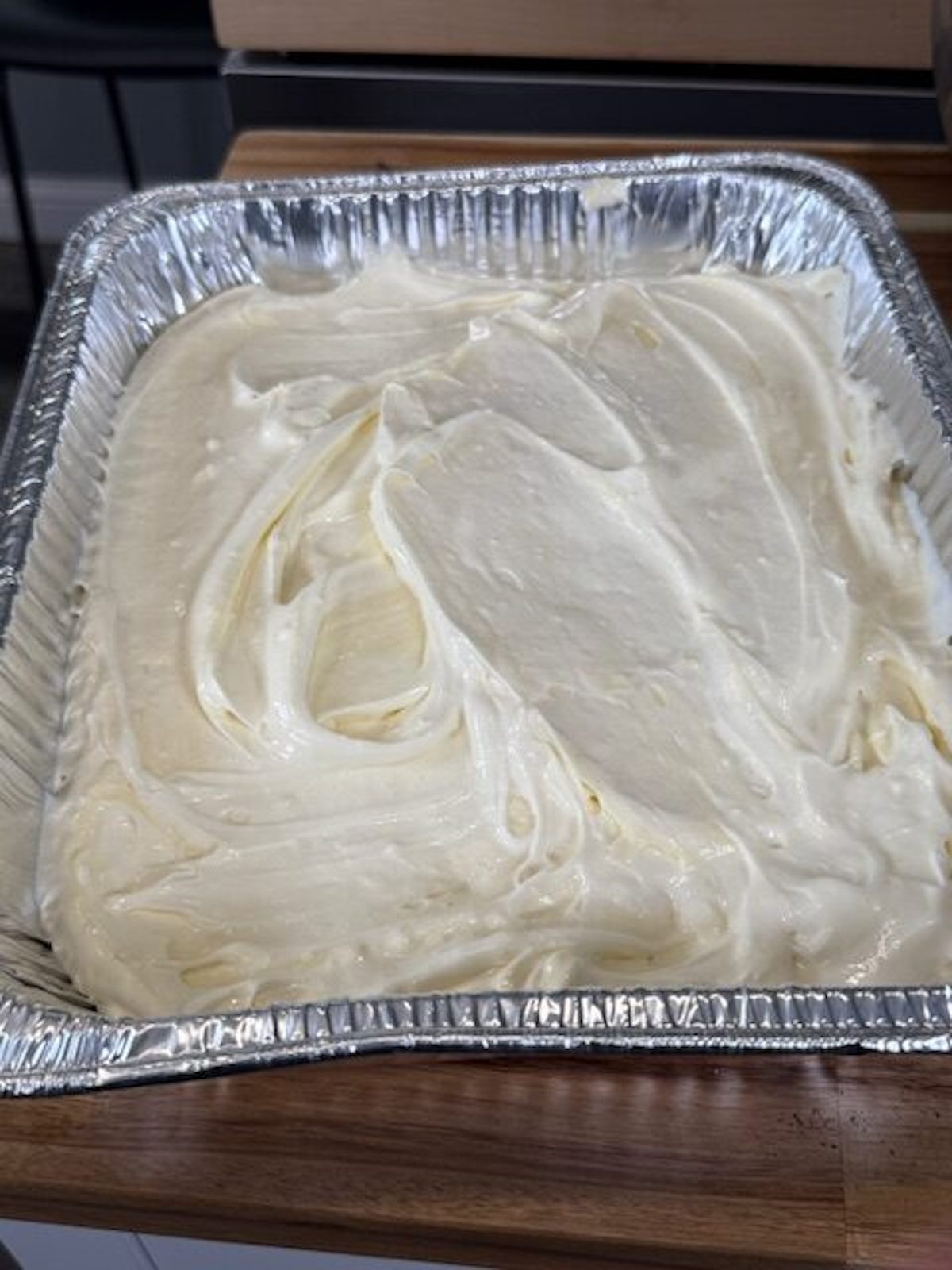 The vanilla pudding mixture is spread into an aluminum pan.