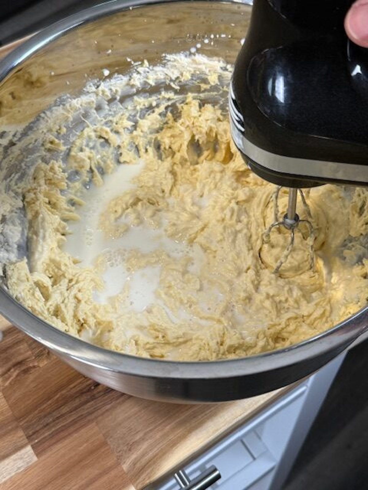 A hand mixer is mixing banana pudding mix in a large metal bowl.