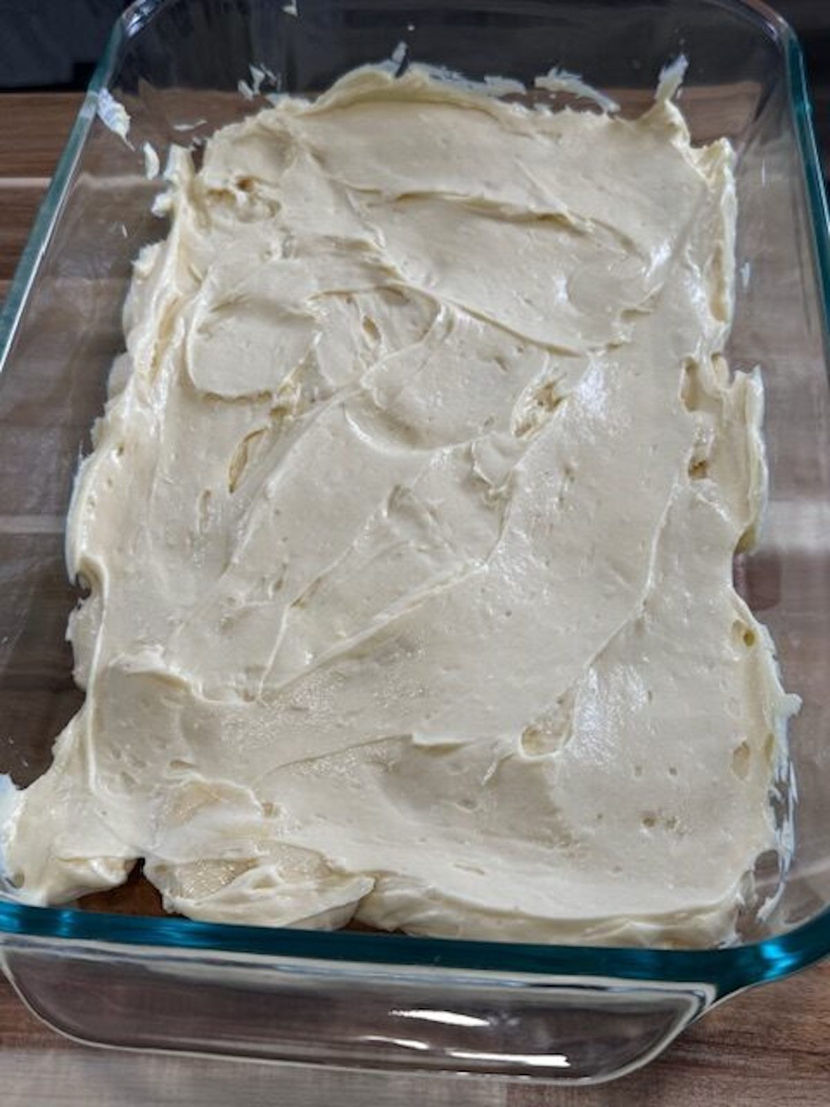 Banana pudding mixture is spread over top of bananas and cookies in a baking dish.