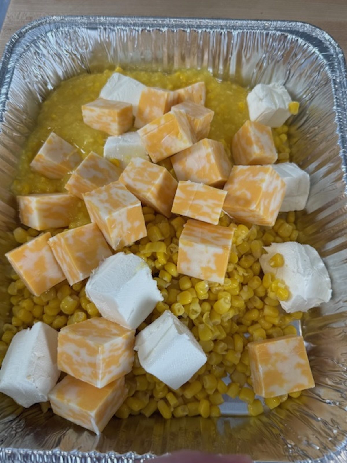 Cubes of cream cheese and colby jack on top of the corn mixture in the silver tray.