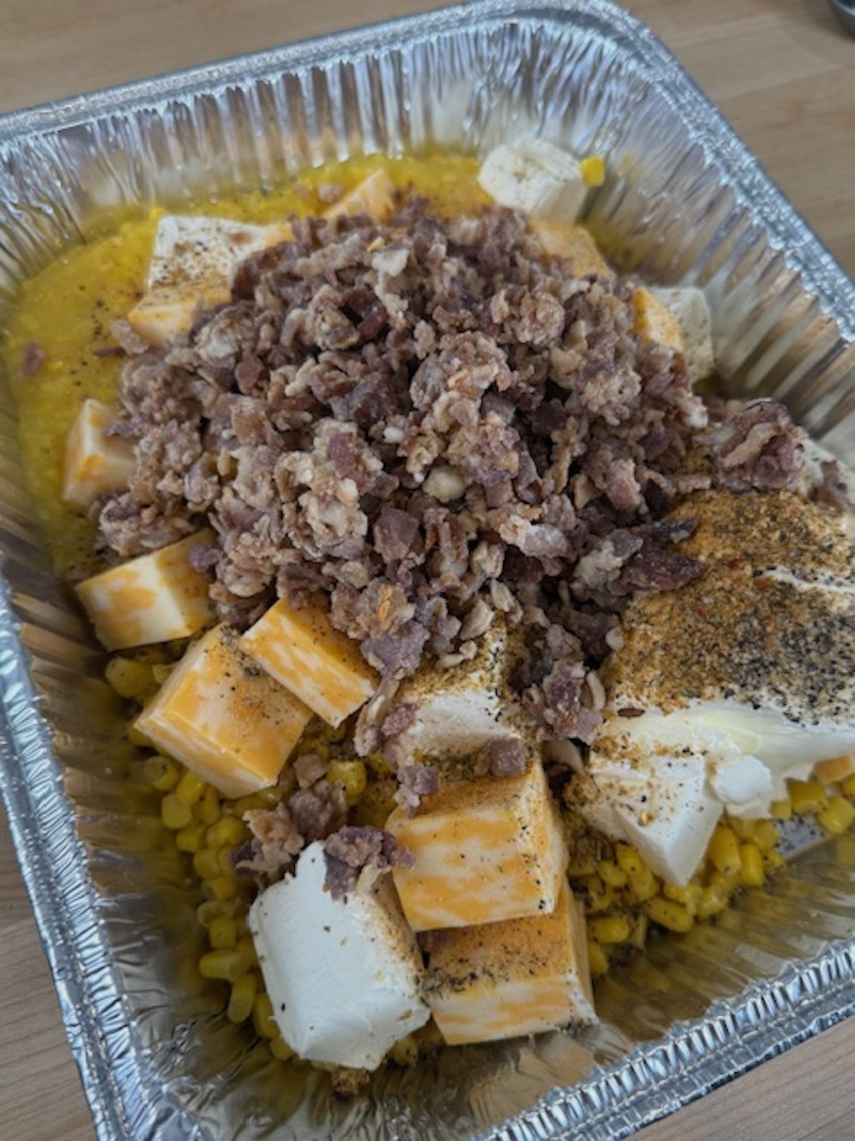Cooked bacon on top of the cheese and corn in the silver tray.
