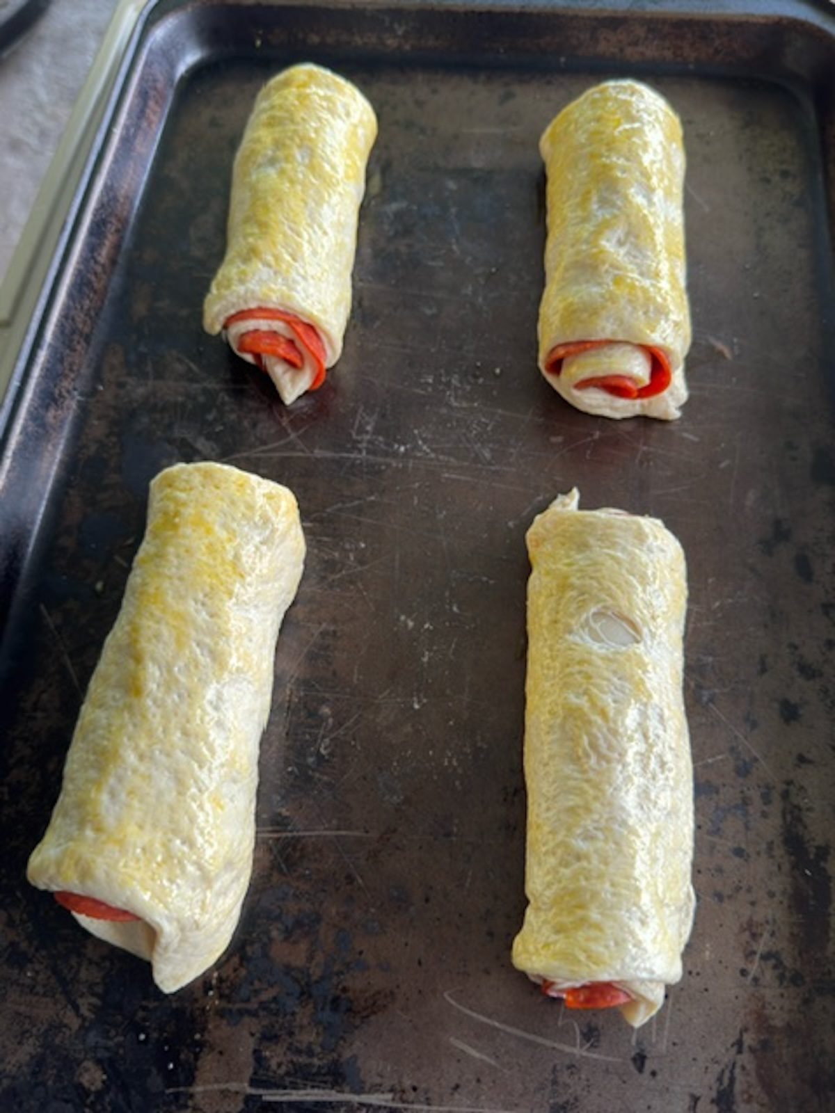 Rolled pepperoni rolls on a baking sheet ready to bake.