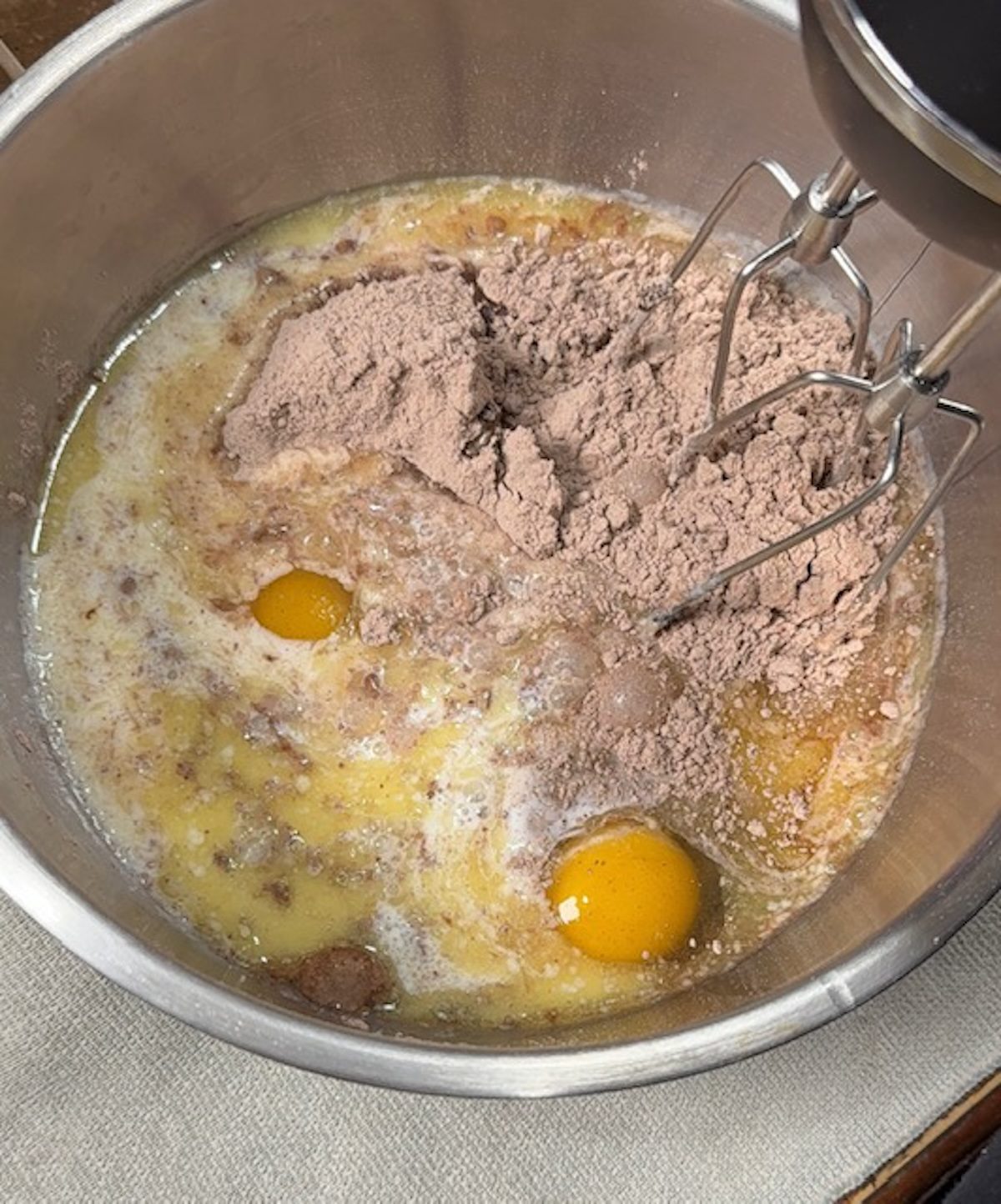 A hand mixer is mixing in a metal bowl the cake mix, eggs, and oil.