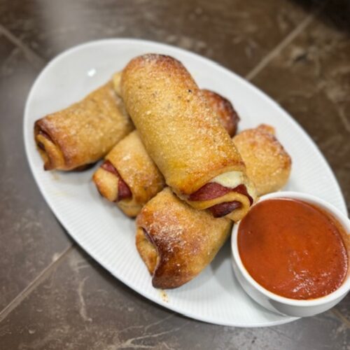 Baked pepperoni rolls on a platter with marinara sauce for dipping.