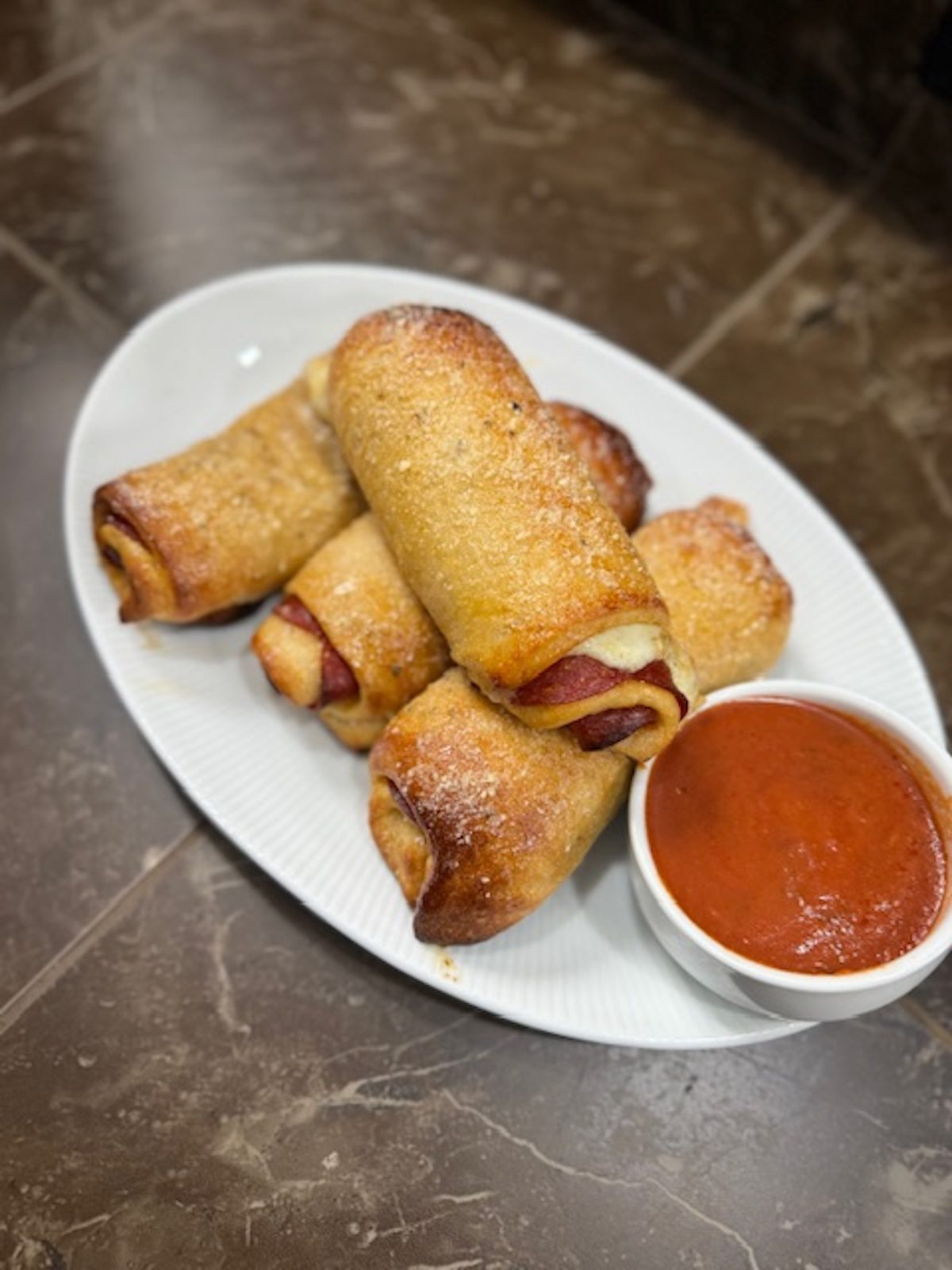 Baked pepperoni rolls on a platter with marinara sauce for dipping.