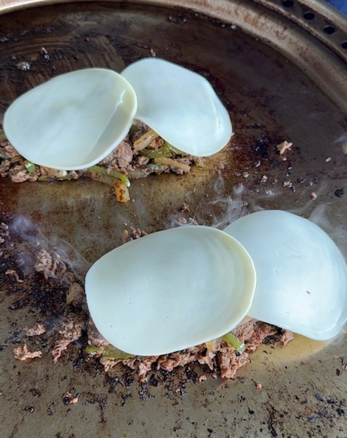 Two pieces of provolone on top of two piles of griddled beef.