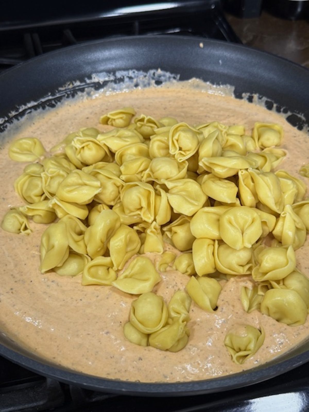 Cheese tortellini being added into the marry me chicken pasta sauce.