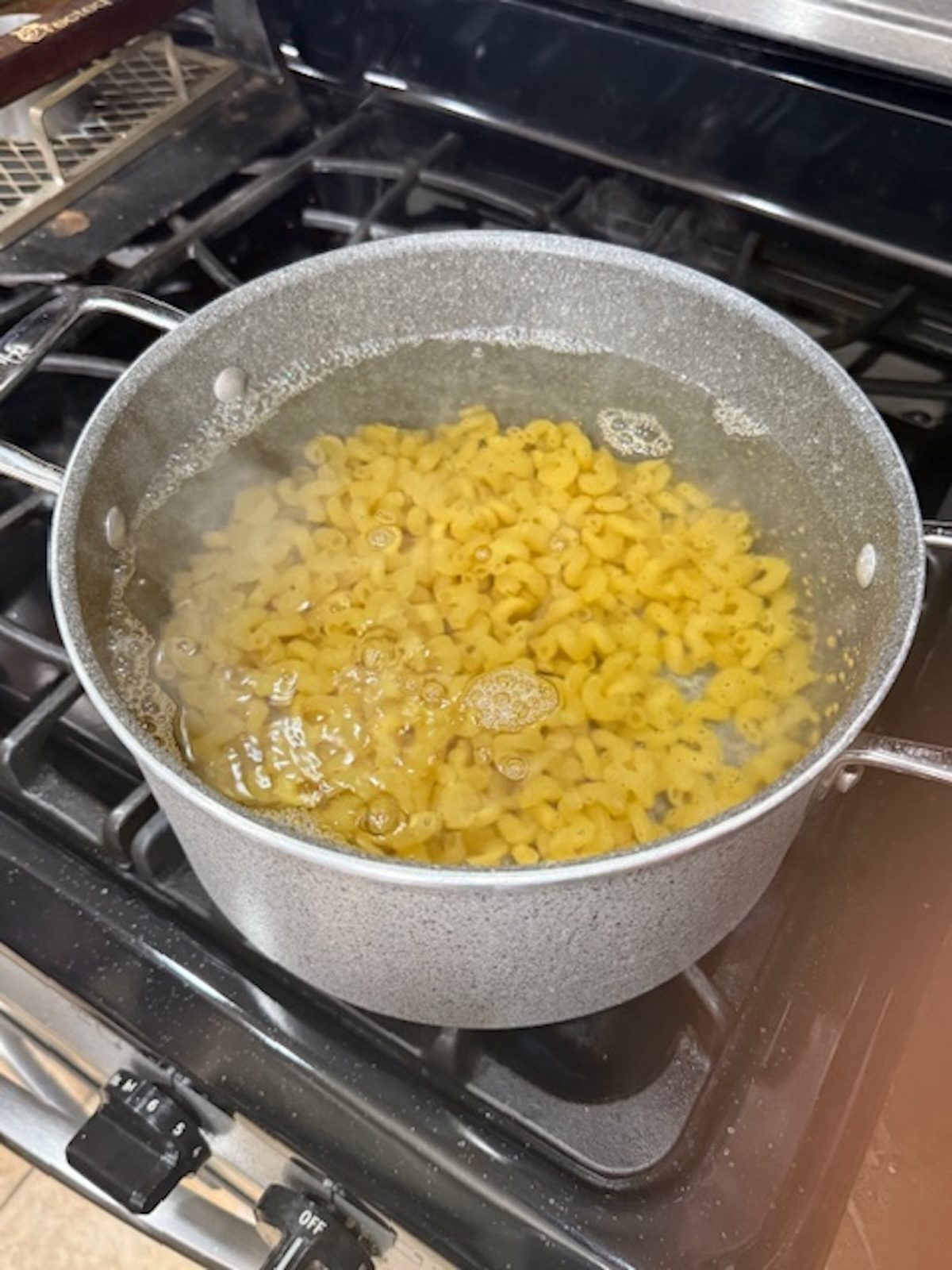 Noodles boiling in a large pot on the stovetop for slow cooker mac and cheese.