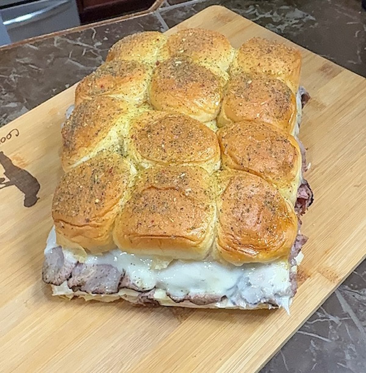 Baked beef and gravy sliders on a wooden cutting board.